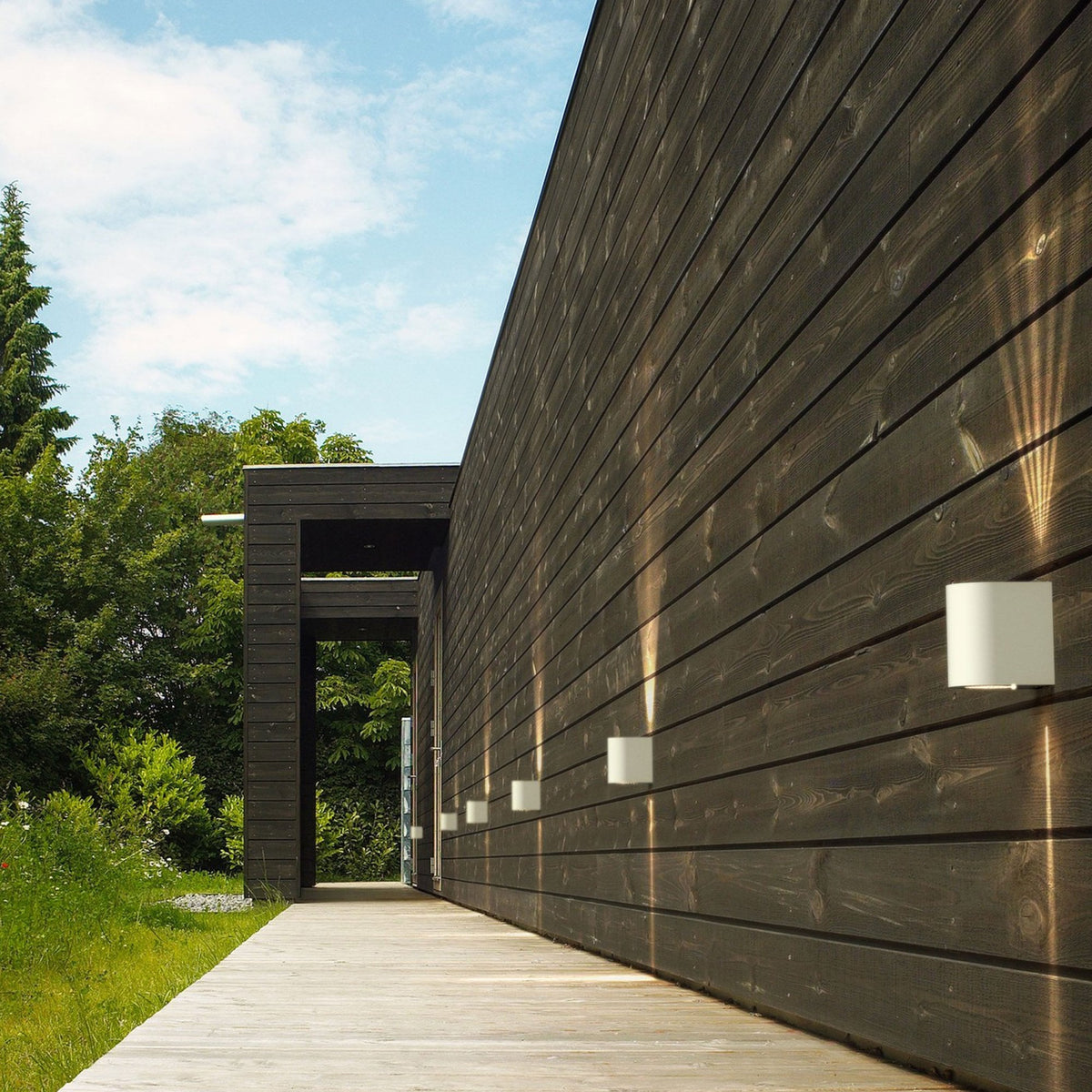 Several outdoor wall lights illuminate the exterior of a modern building with wooden cladding.