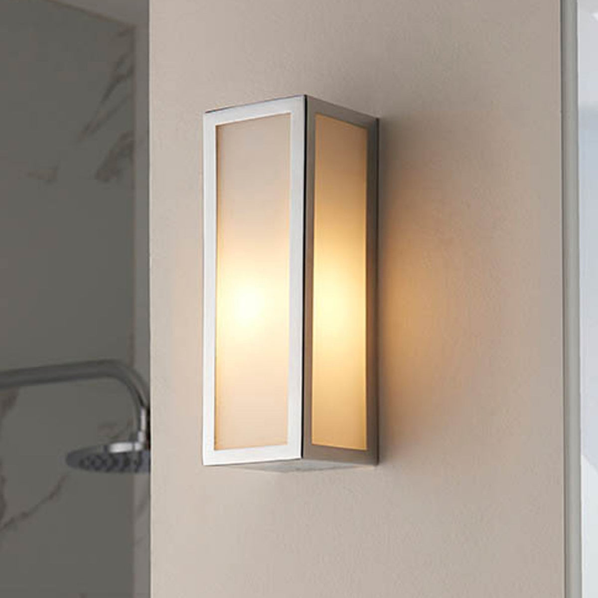 A rectangular wall light with a brushed steel frame and frosted glass panels, emitting a warm glow.