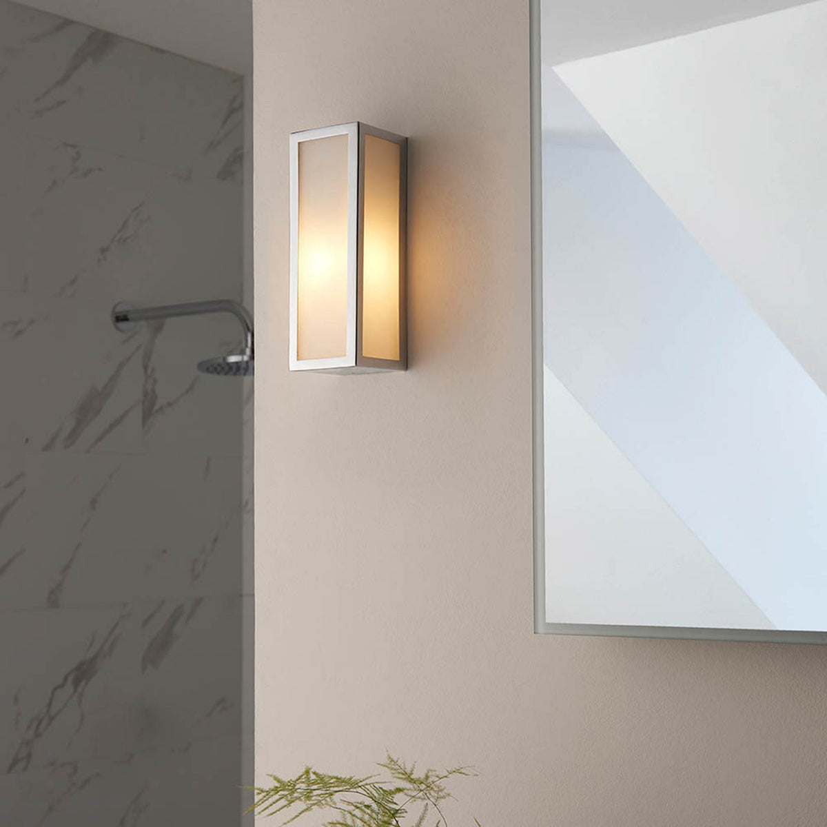 A rectangular wall light with a brushed steel frame and frosted glass panels, next to a mirror.