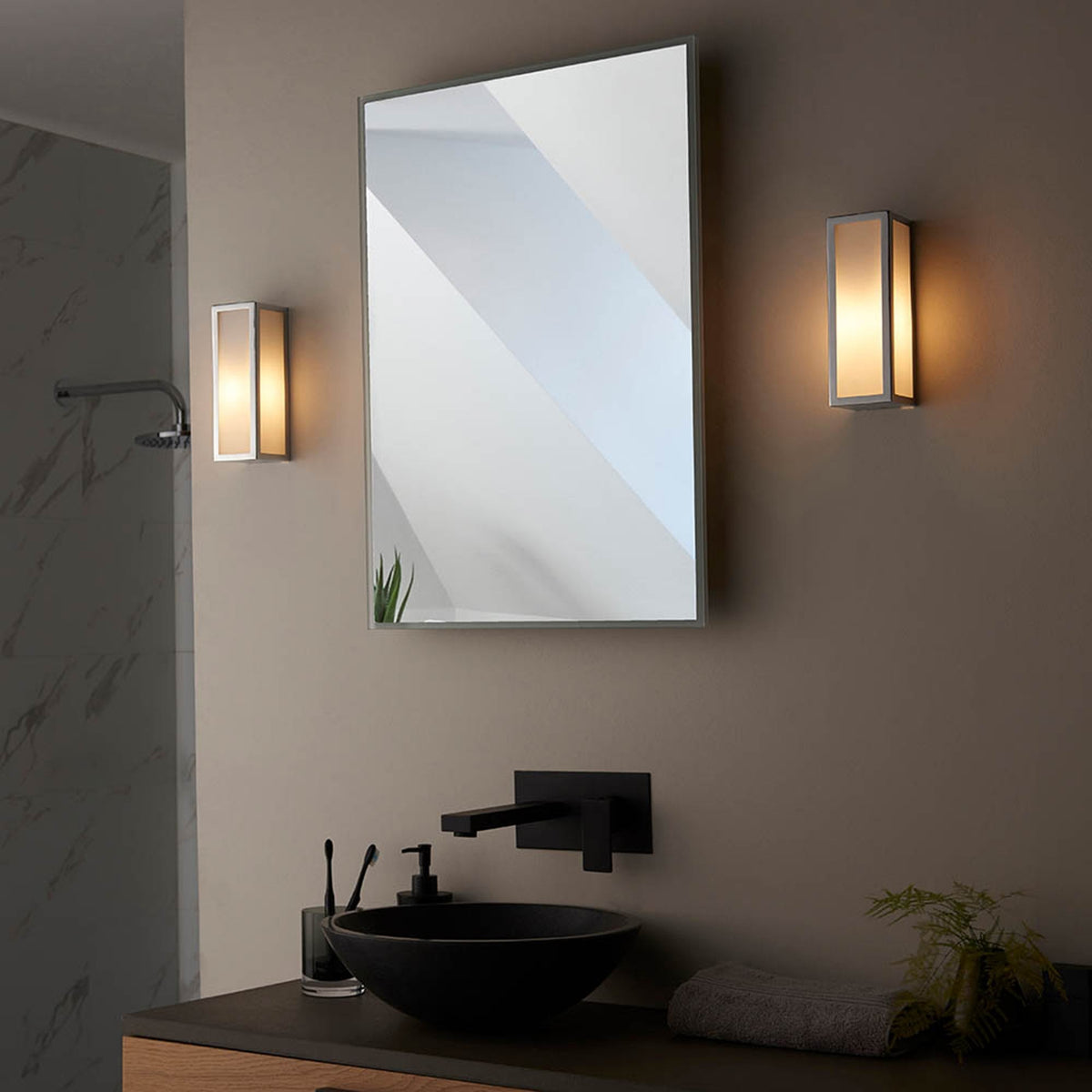 Two rectangular wall lights flank a mirror above a black sink and faucet in a modern bathroom.