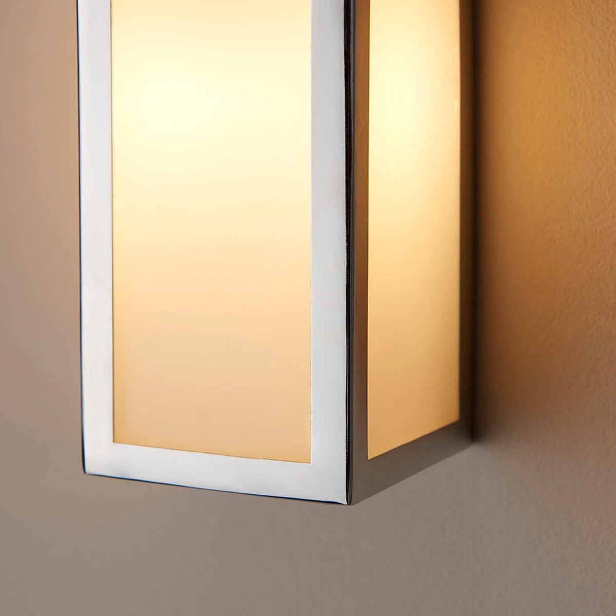 Close-up of a rectangular wall light with a brushed steel frame and frosted glass panels, emitting a warm glow.