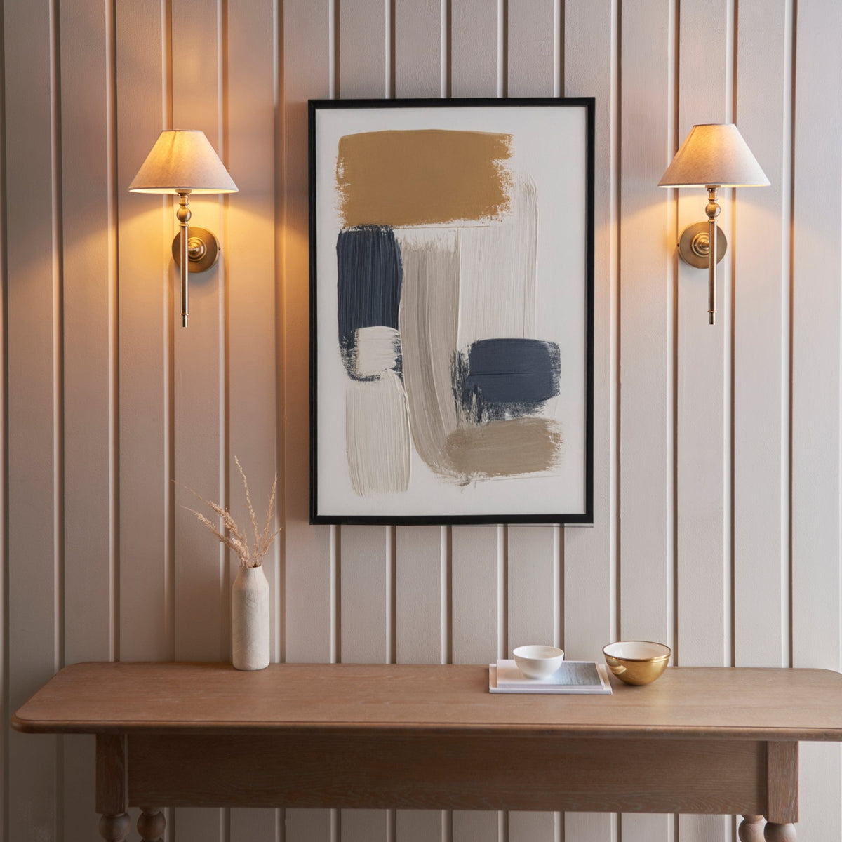 Two brass wall lights flank an abstract painting above a wooden console table.
