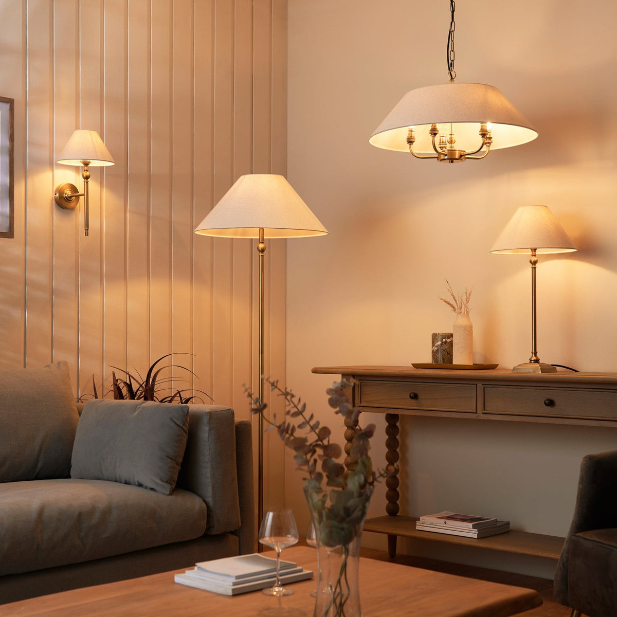 A living room with various brass and cream lighting fixtures, including a wall light, floor lamp, and table lamp.