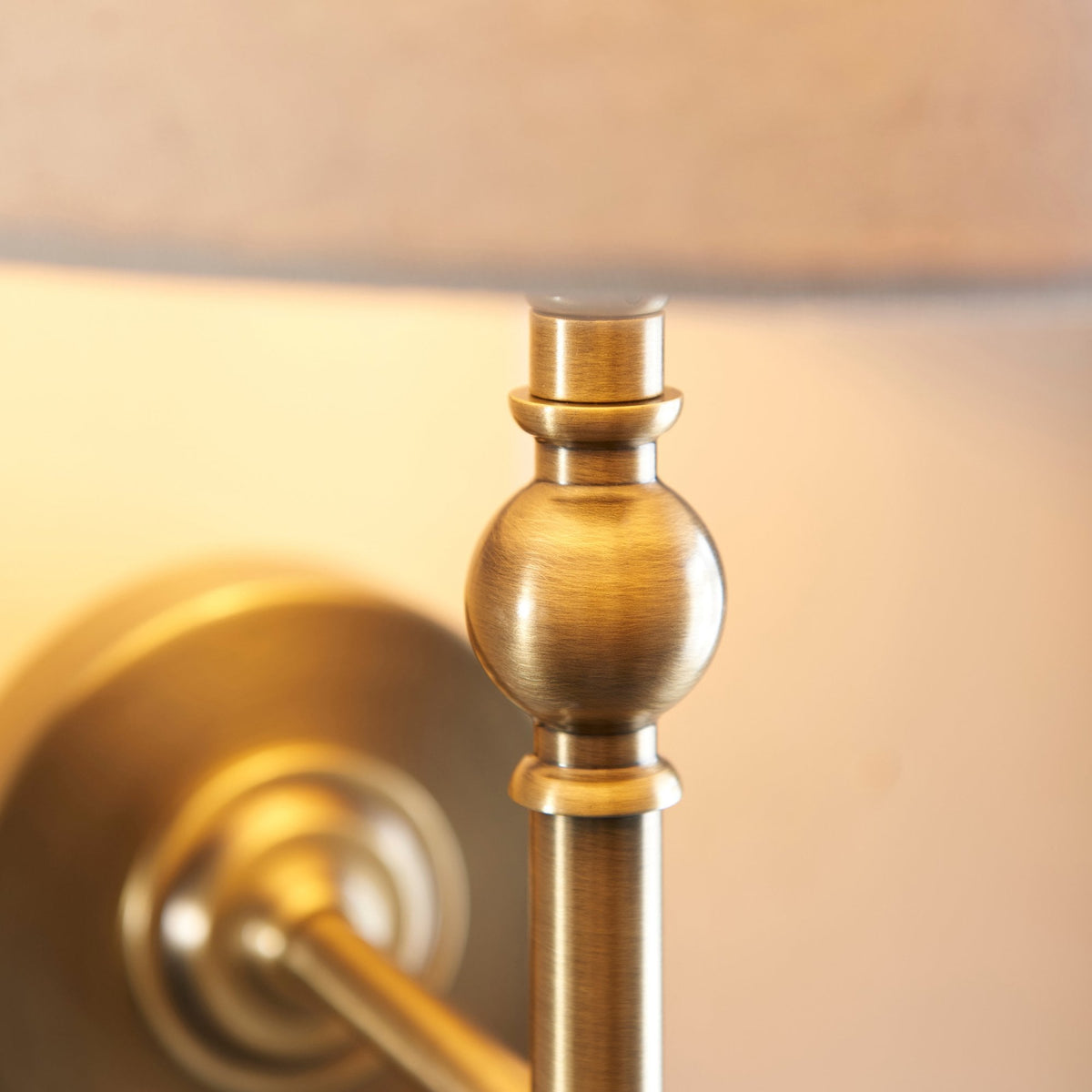 Close-up of the antique brass finish on the stem of a wall light with a cream shade.