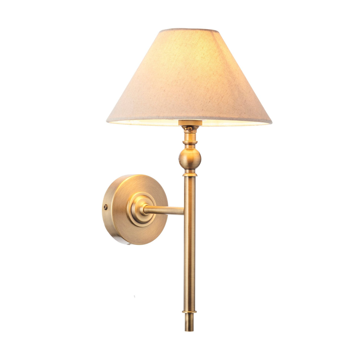 A brass wall light with a cream fabric shade, illuminated against a white background.