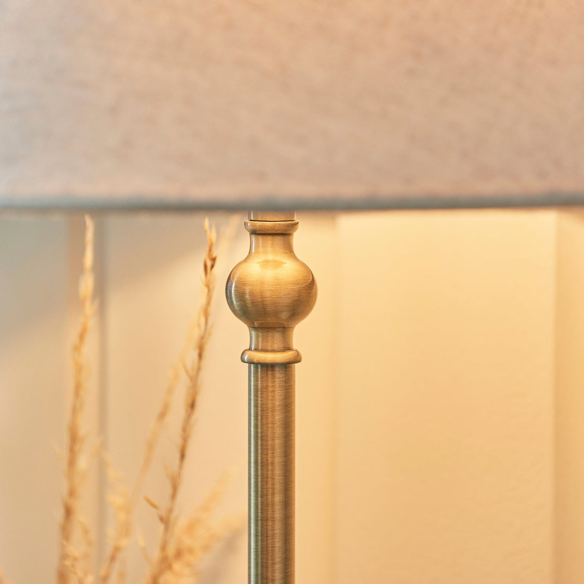 Close-up of the ornate brass stem of a table lamp with a light linen shade.