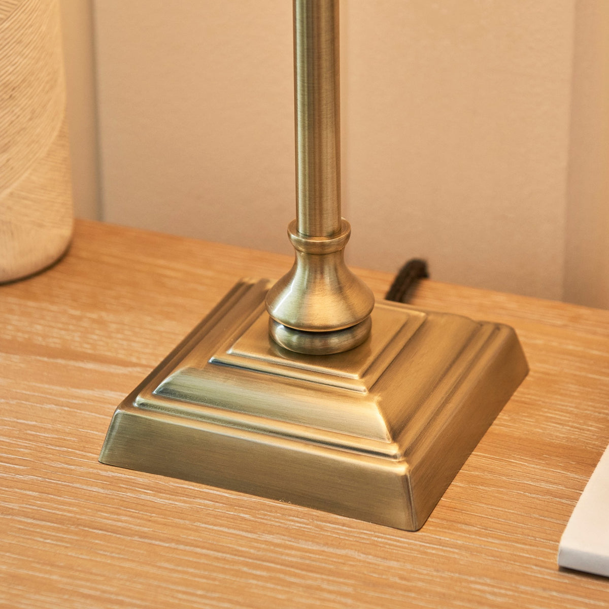 Close-up of the square, antique brass base of a table lamp on a light wooden surface.