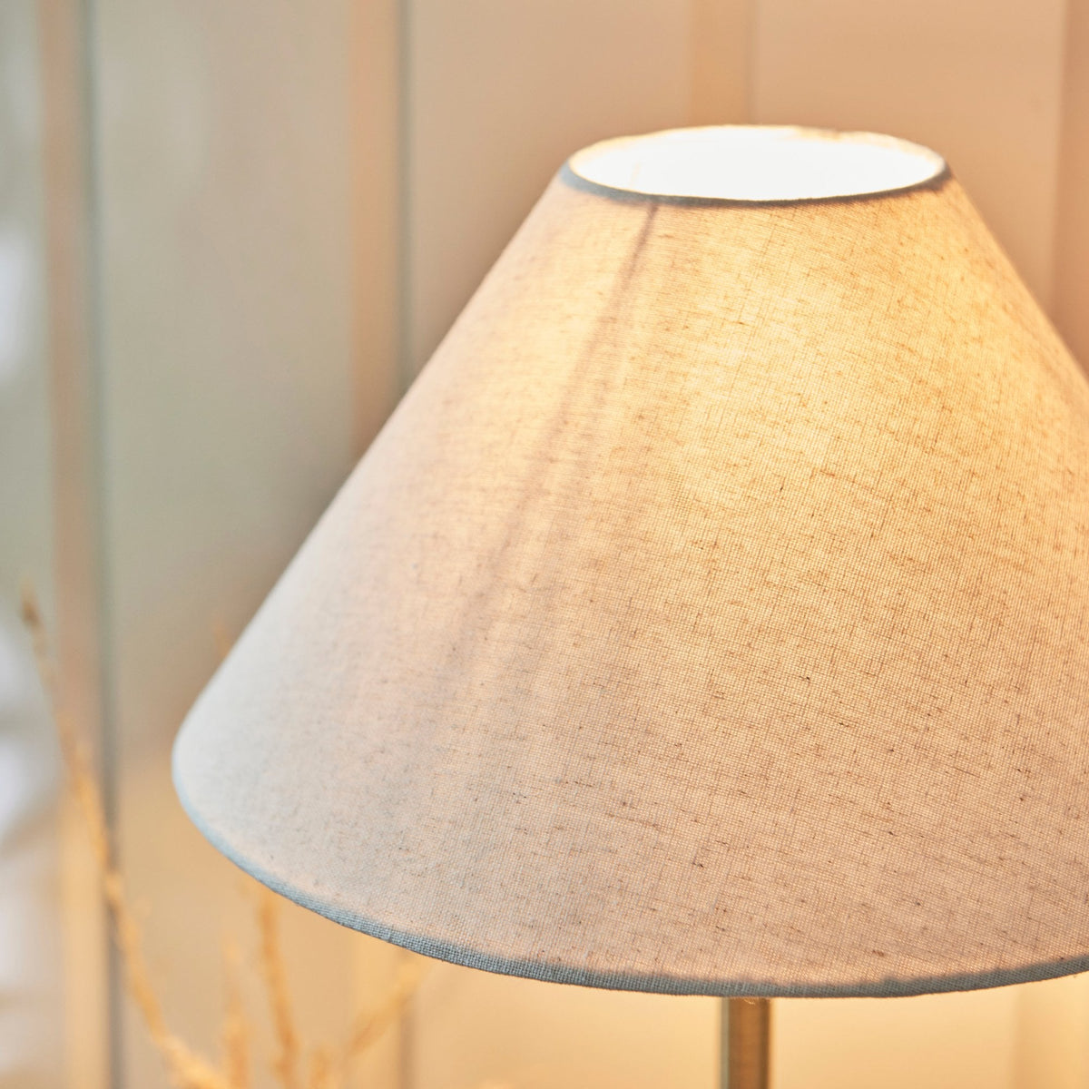Close-up of a light linen lampshade glowing warmly, casting light on a textured wall.