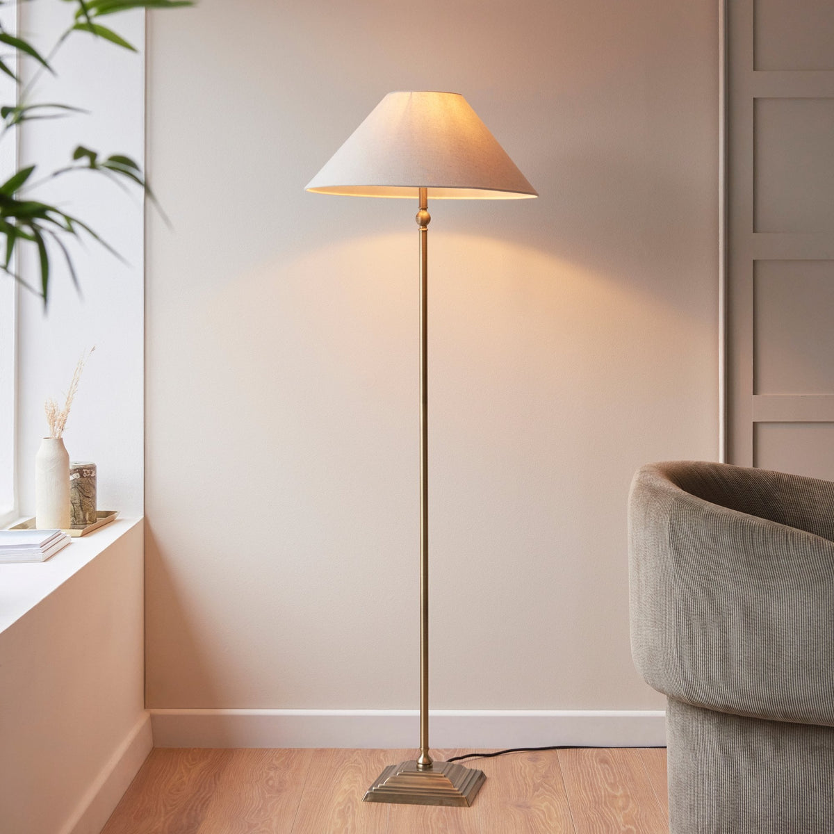 A tall, brass floor lamp with a cream-colored shade illuminates a cozy living room corner.
