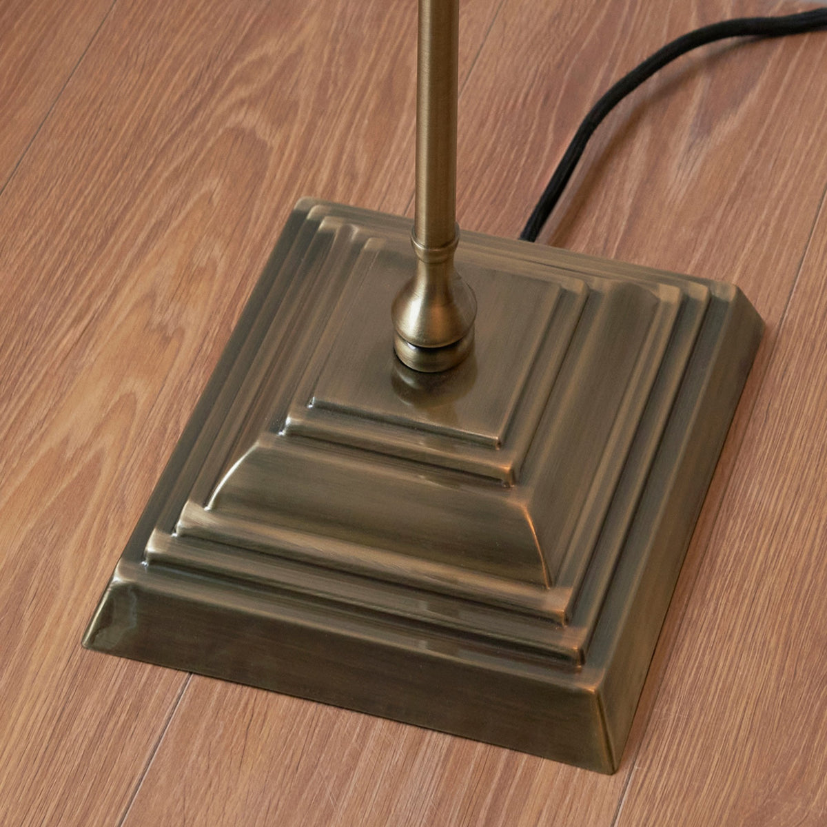 Close-up of the square, tiered brass base of a floor lamp on a wooden floor.