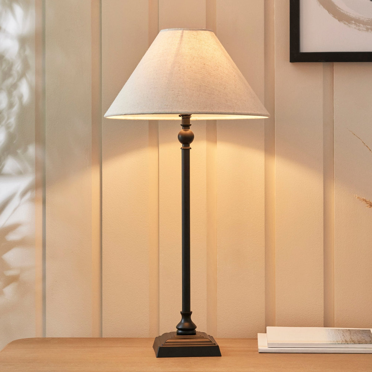 A close-up shot of an antique black table lamp on a wooden desk with a grey lampshade.