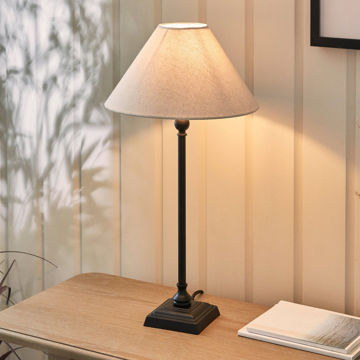 An antique black table lamp with a grey lampshade illuminates a wooden desk.