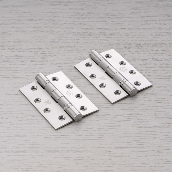 Pair of satin chrome door hinges with fixing holes on a light wood surface.