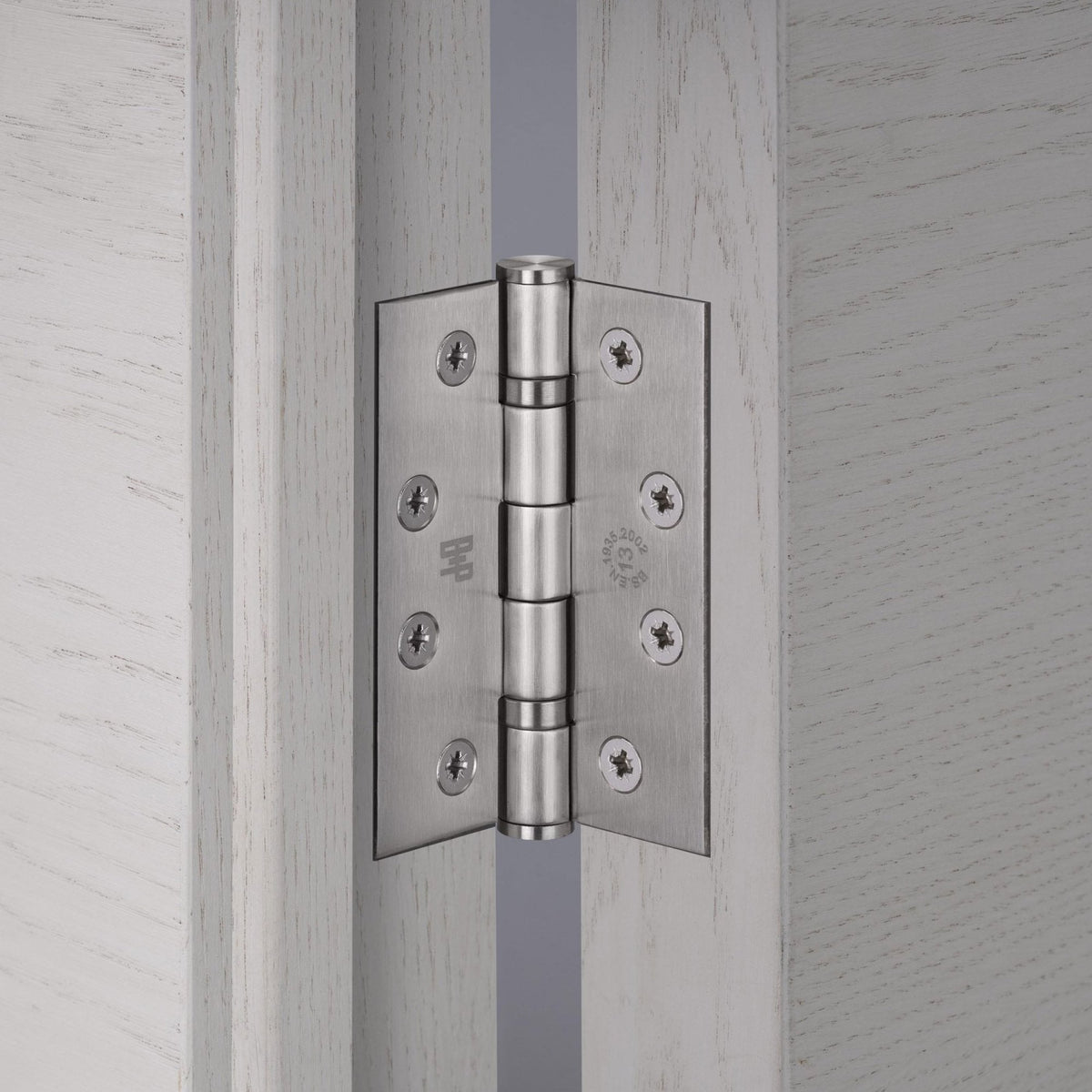 Satin chrome door hinge installed on a light wood door frame.