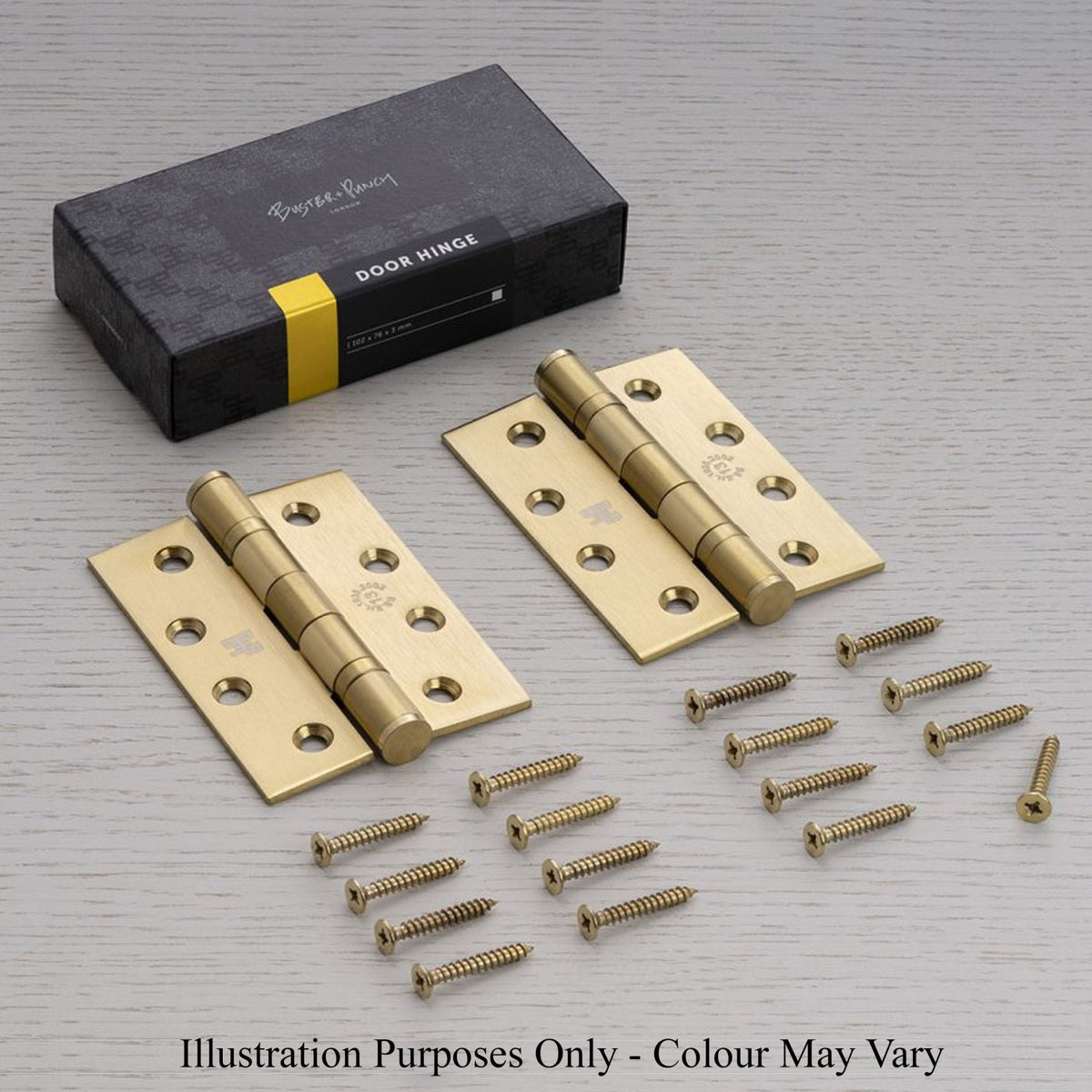 Pair of brass door hinges with screws and packaging on a light wooden surface.