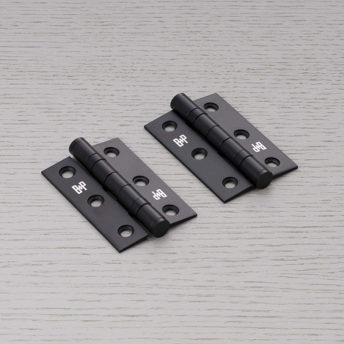 Two matt black door hinges with rounded barrels and six screw holes each.