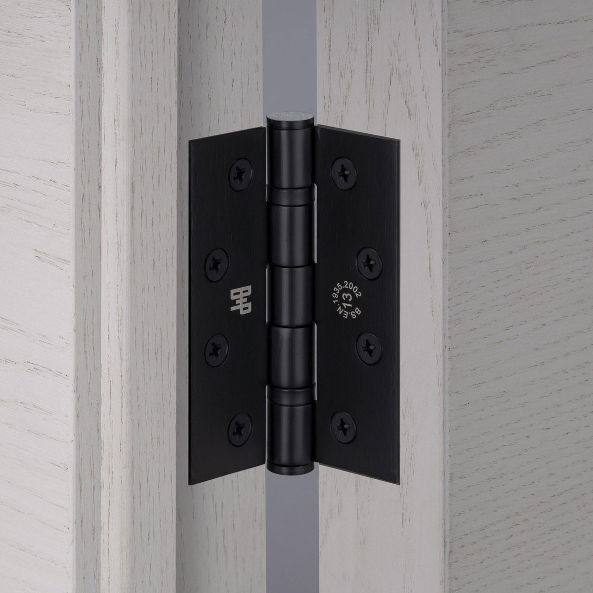 Close-up of a matt black door hinge installed on a light-coloured wooden door.
