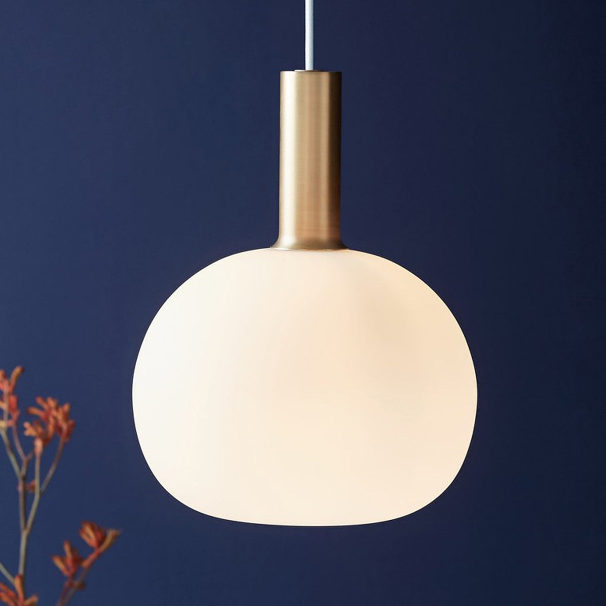 A close-up of the large white pendant light with a brass neck, hanging against a dark blue wall.