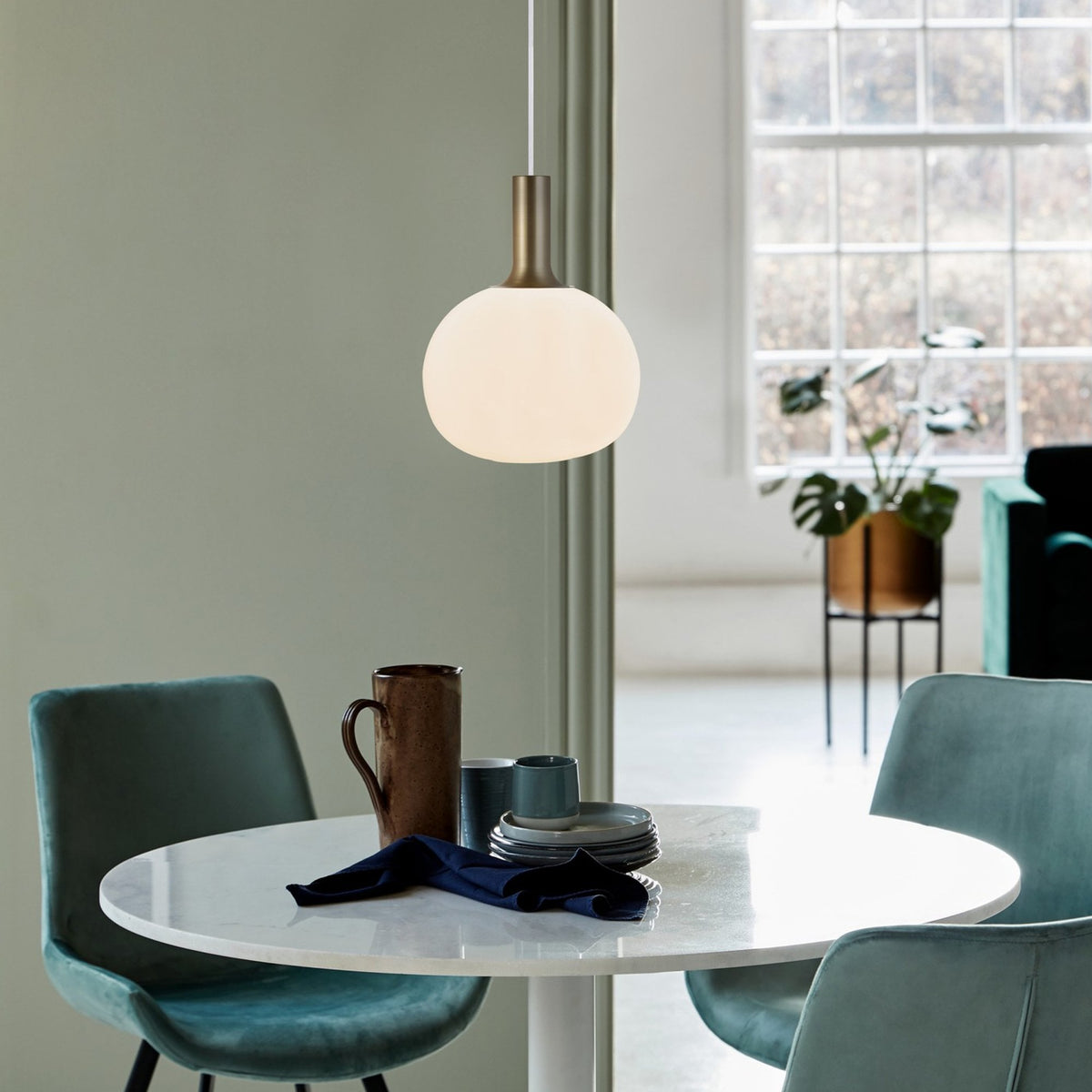 A large white pendant light with a brass neck, hanging above a white dining table with chairs.