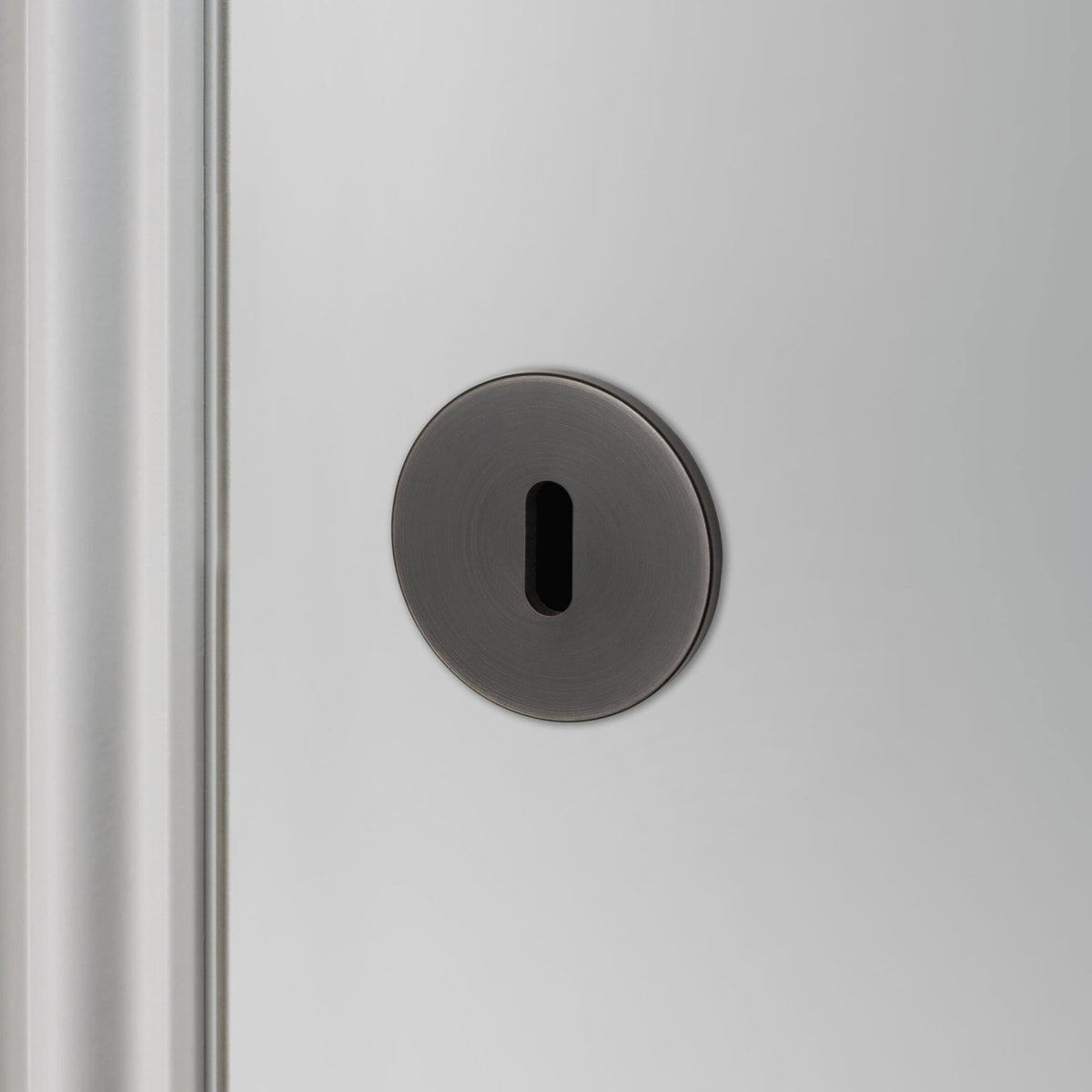 A close-up of a black keyhole escutcheon on a light grey door.