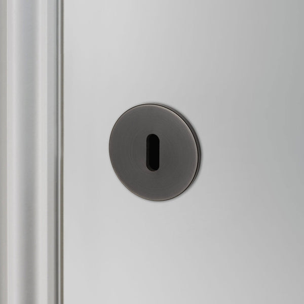 A close-up of a black keyhole escutcheon on a light grey door.