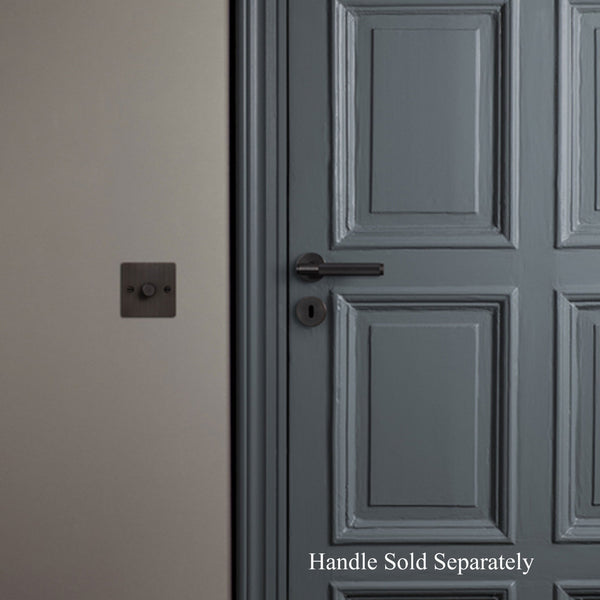 A black keyhole escutcheon on a grey door with a light switch on the wall.