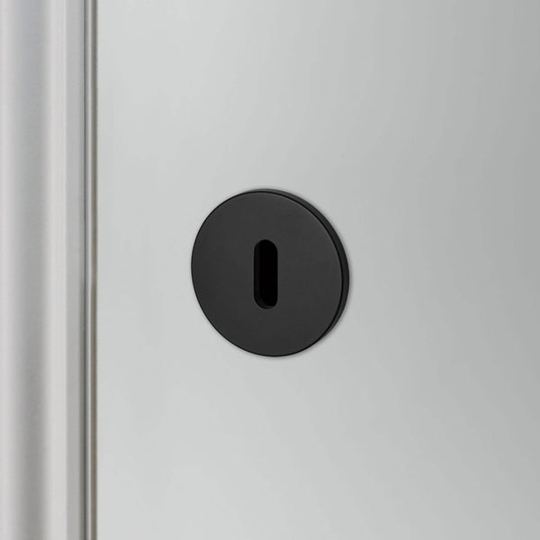 A close-up of a matte black keyhole cover on a light-coloured door.