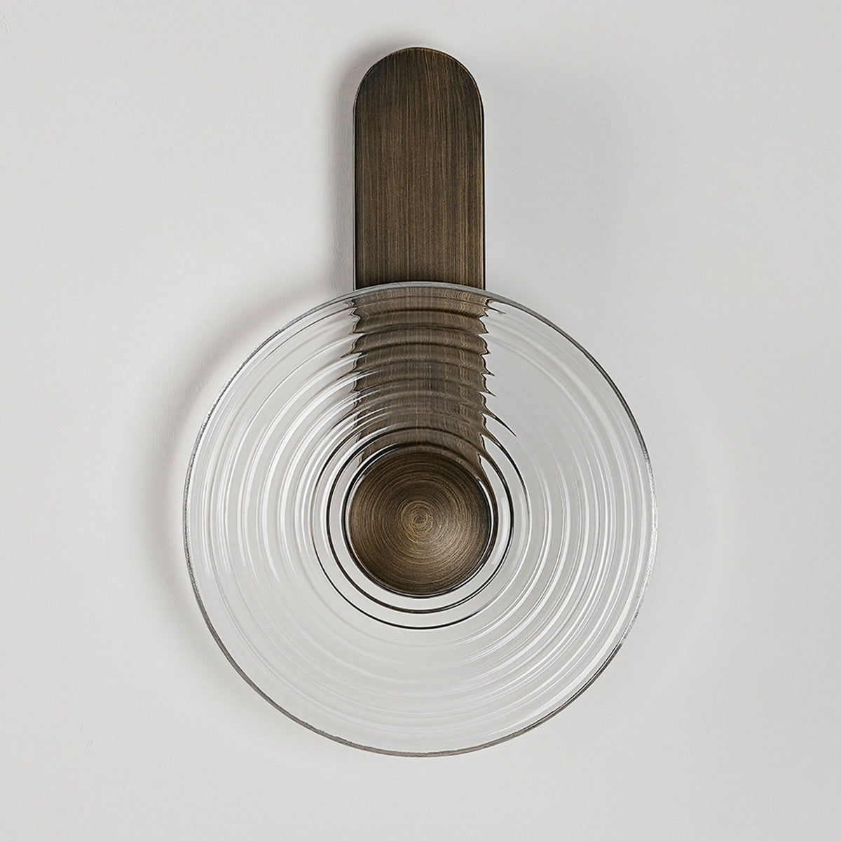 A modern wall lamp with a round, clear, ribbed glass shade and a dark metal base, unlit.