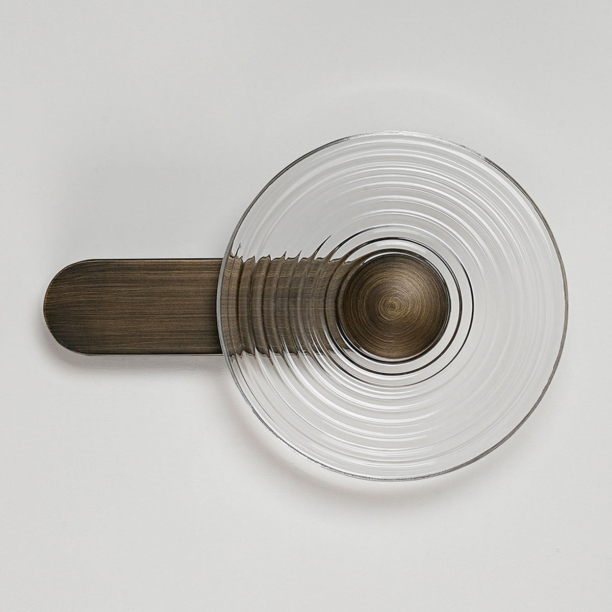 A modern wall lamp with a round, clear, ribbed glass shade and a dark metal base, unlit.