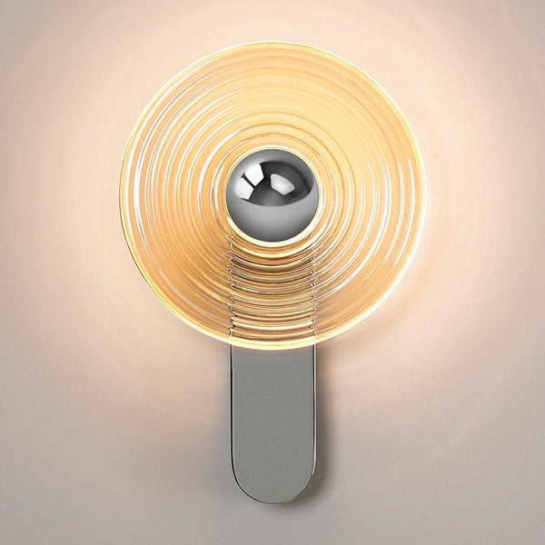 A contemporary wall lamp with a radiant amber glass disc and a sleek silver base, illuminated.