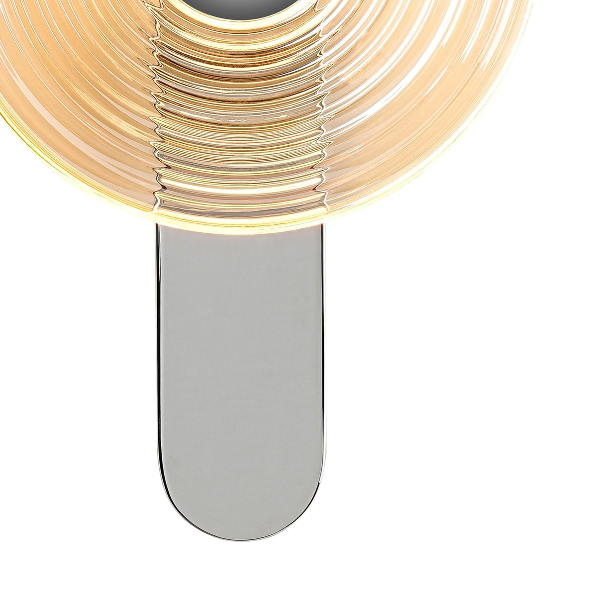 Close-up of the illuminated amber glass shade and silver base of a modern wall lamp.