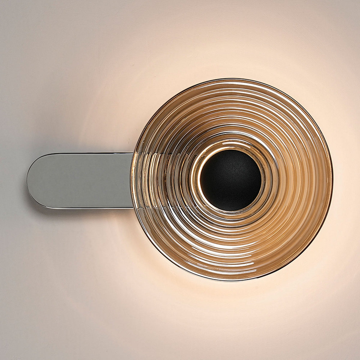 A modern chrome wall light with a circular, ridged shade, illuminated and fixed horizontally.