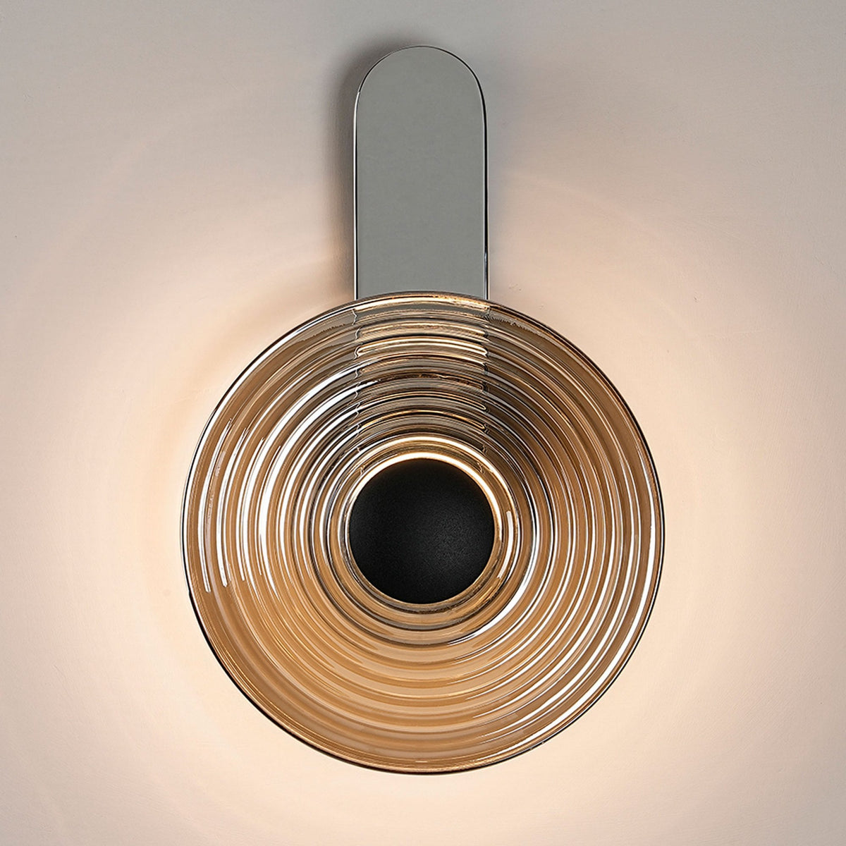 A modern chrome wall light with a circular, ridged shade, illuminated and fixed vertically.