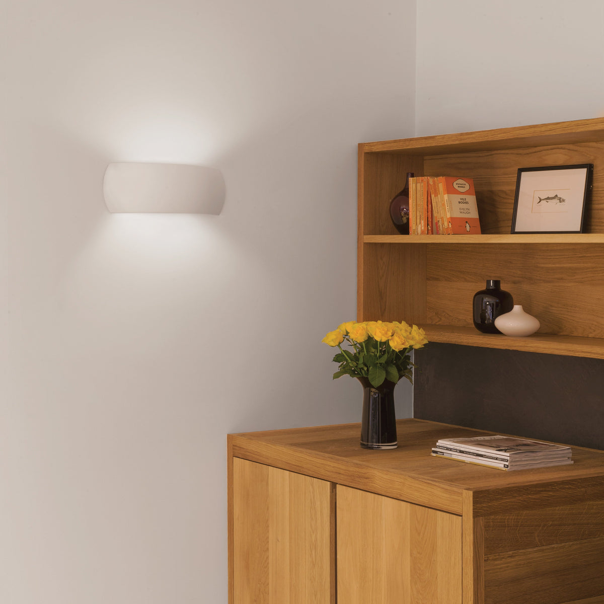 White wall light illuminating a corner with a wooden cabinet and shelves holding books and decor