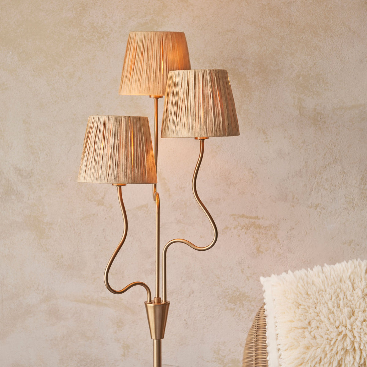 Close-up of the three pleated raffia lamp shades on a brass floor lamp, casting a warm glow.