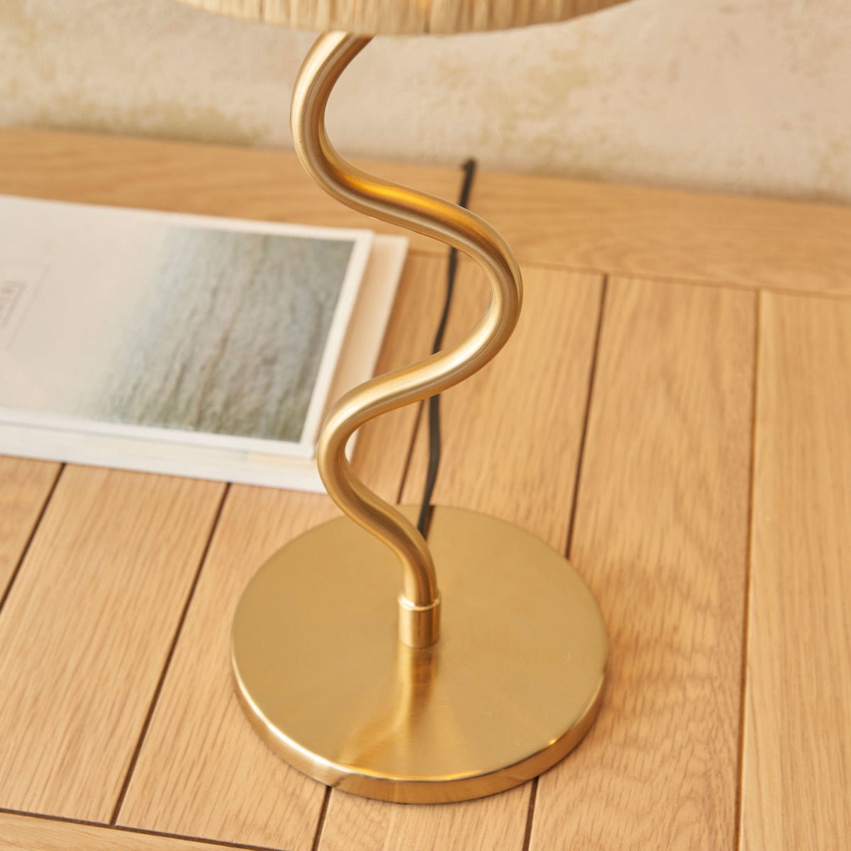 Close-up of the gold wavy stem and round base of a table lamp on a wooden surface.