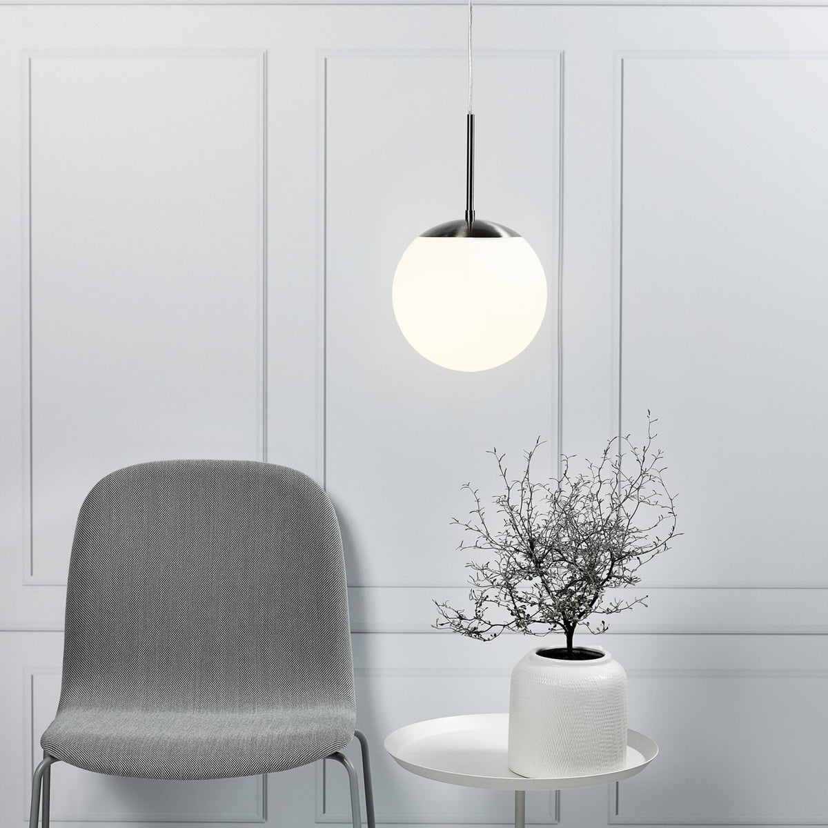 A pendant light with a spherical white shade hanging above a white side table and grey chair.