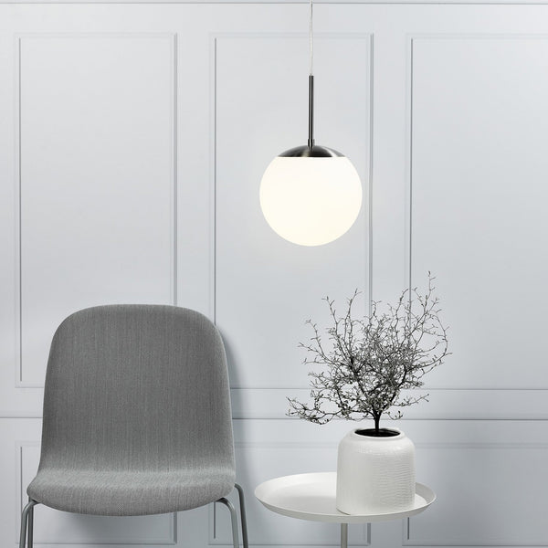 A pendant light with a spherical white shade hanging above a white side table and grey chair.