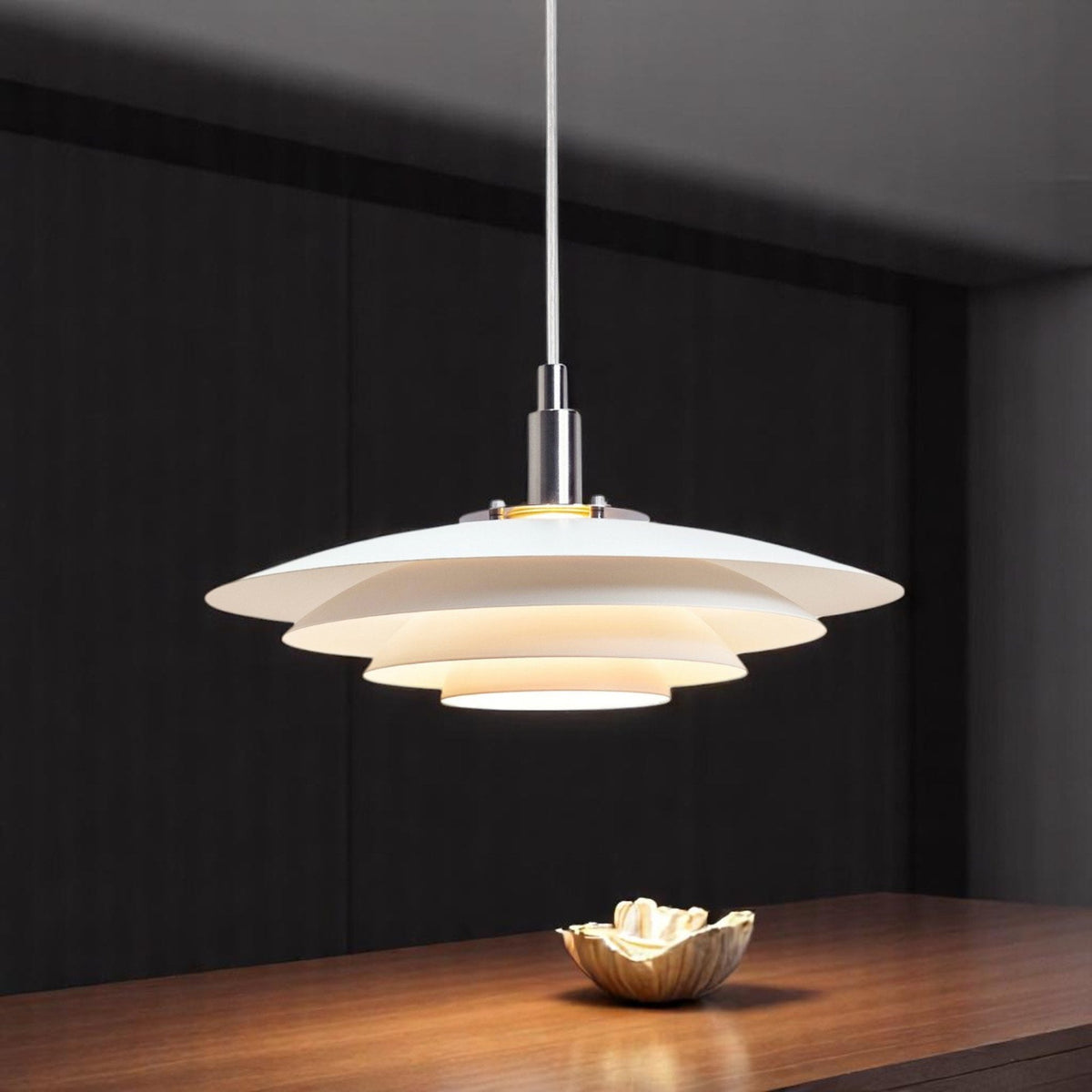A contemporary white tiered pendant light illuminates a wooden table with a decorative bowl.