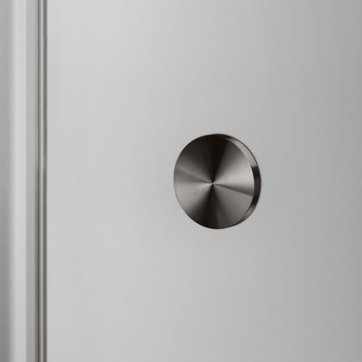 A recessed dark door stopper is flush with a light grey wall.