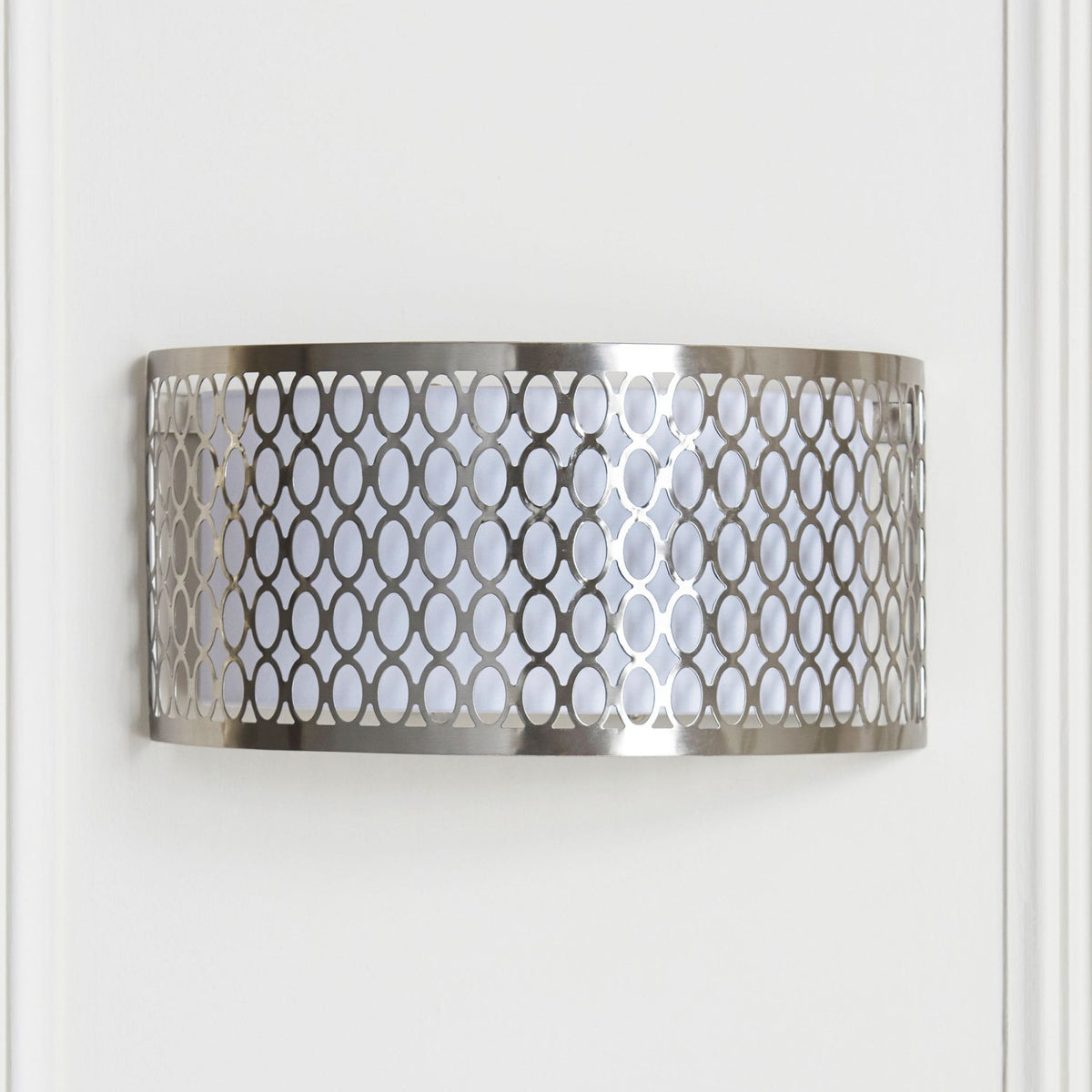 A brushed chrome wall light with an intricate oval pattern, mounted horizontally on a white wall.