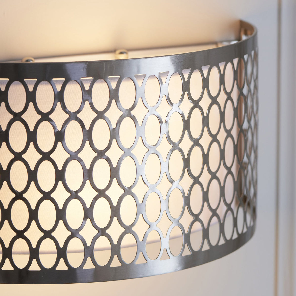 A close-up view of the brushed chrome wall light, highlighting its intricate oval pattern and warm illumination.