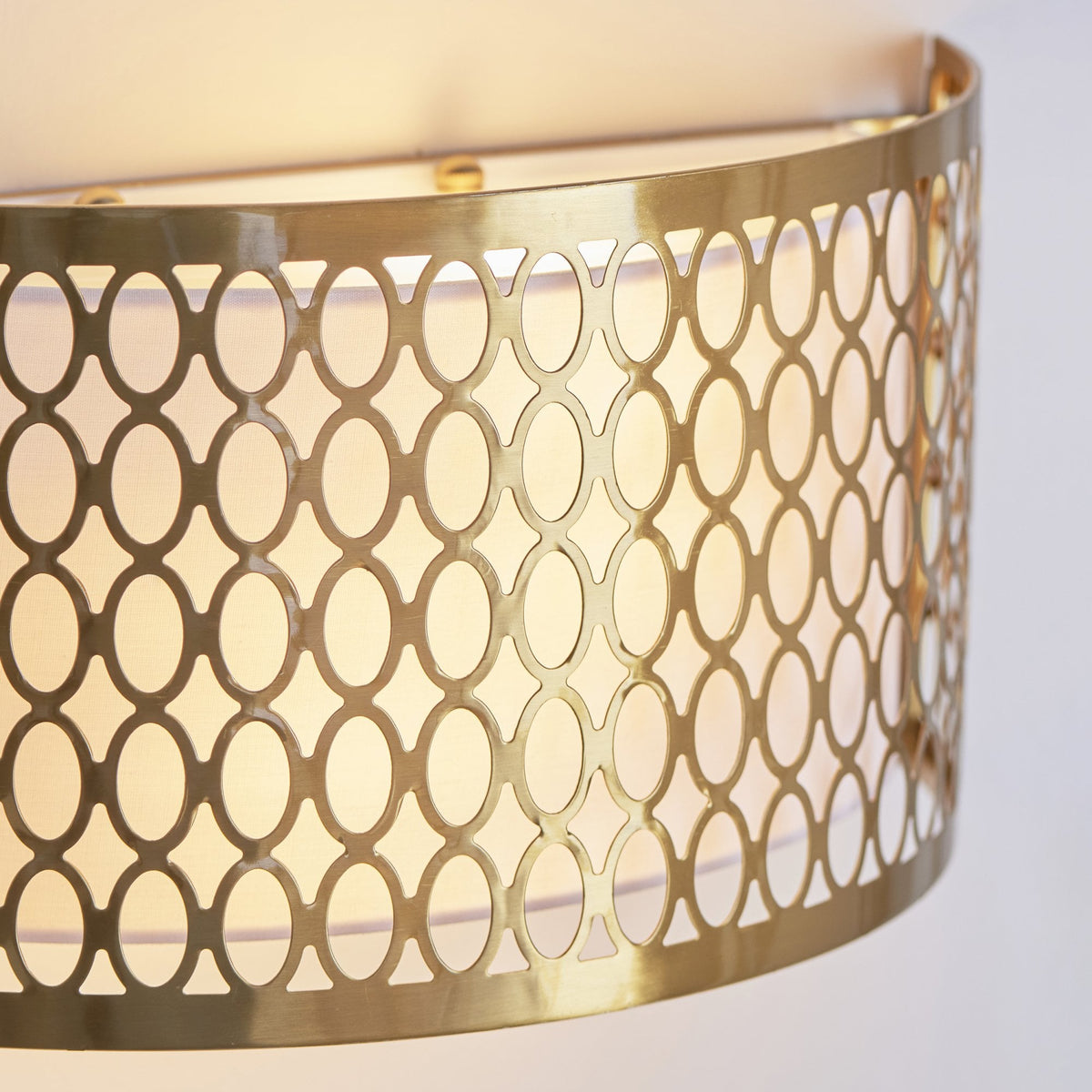 Close-up of the gold wall light, highlighting the intricate oval pattern and the soft glow from within.