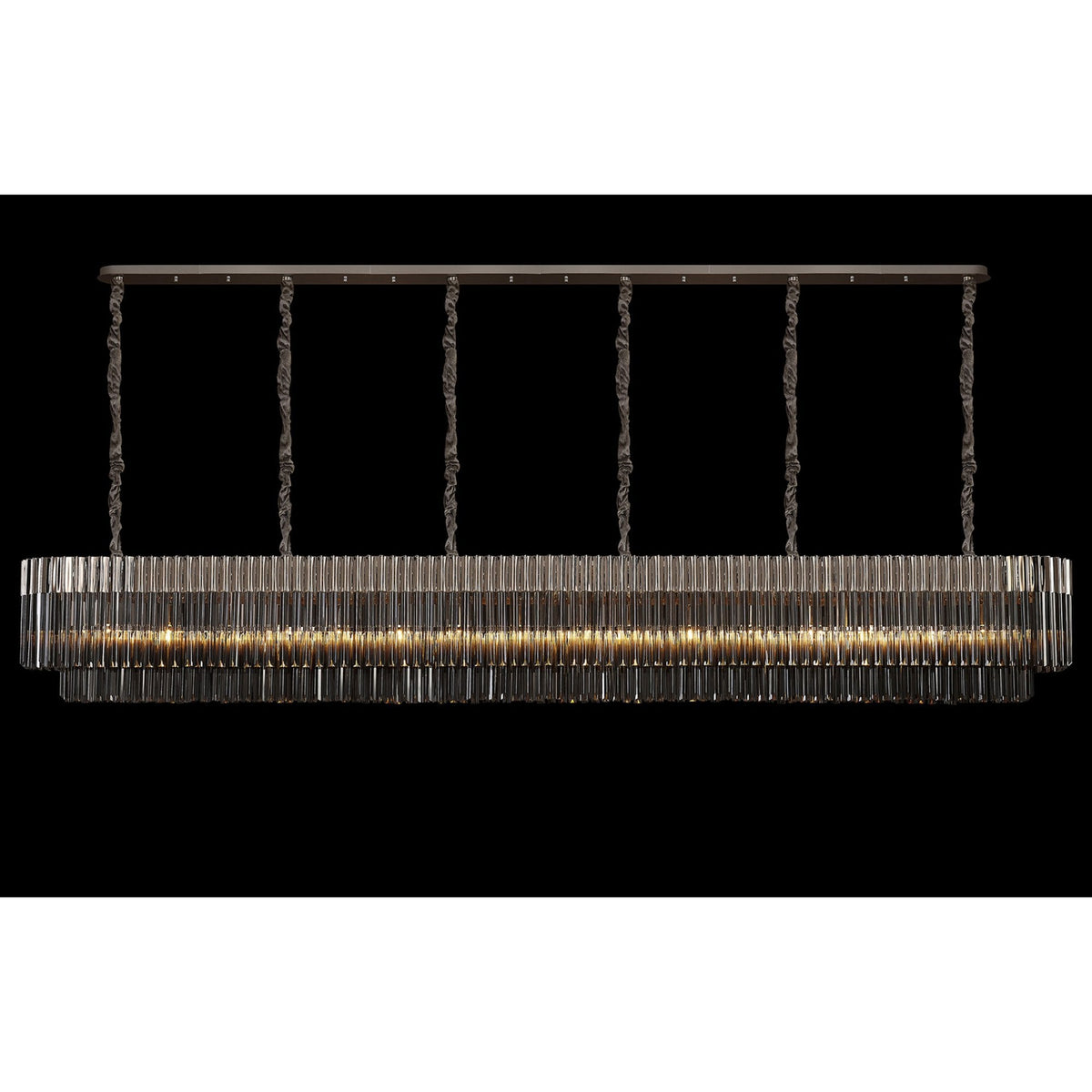 A long, rectangular chandelier with multiple tiers of vertical glass rods, glowing brightly on a black background.