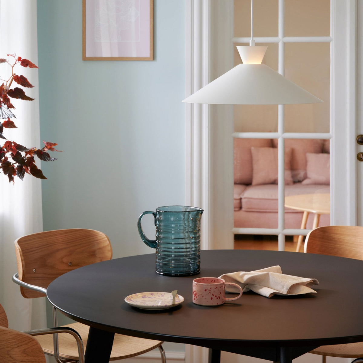 A white pendant light hanging over a dark table with mugs and a jug, in a modern dining room.