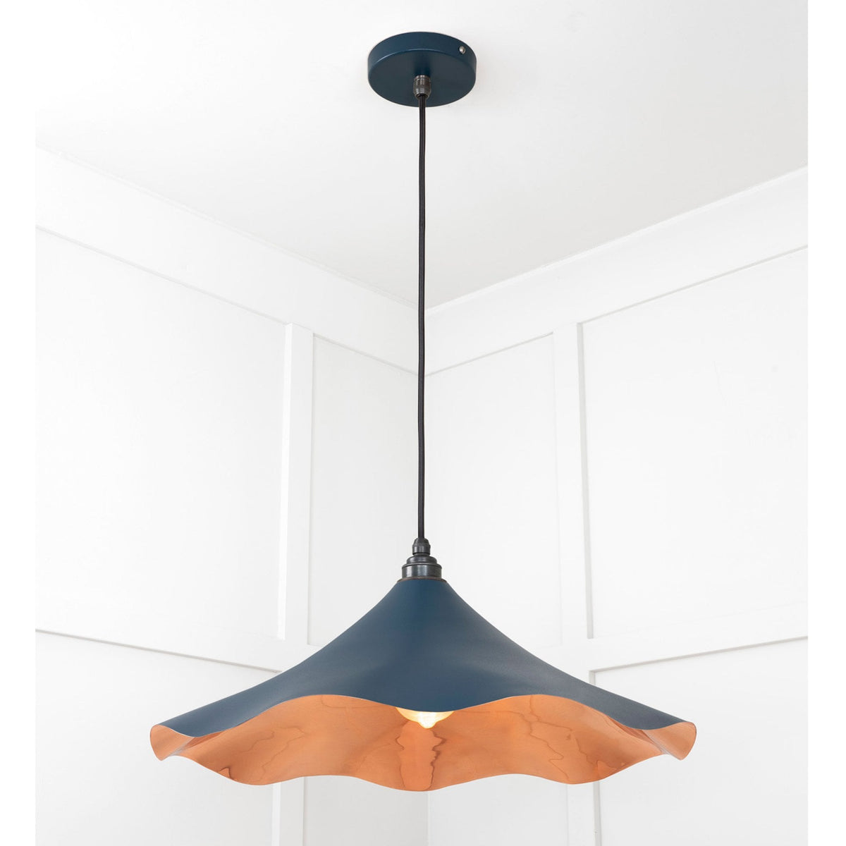 A dark blue and copper pendant light with a wavy rim hangs from a white ceiling.