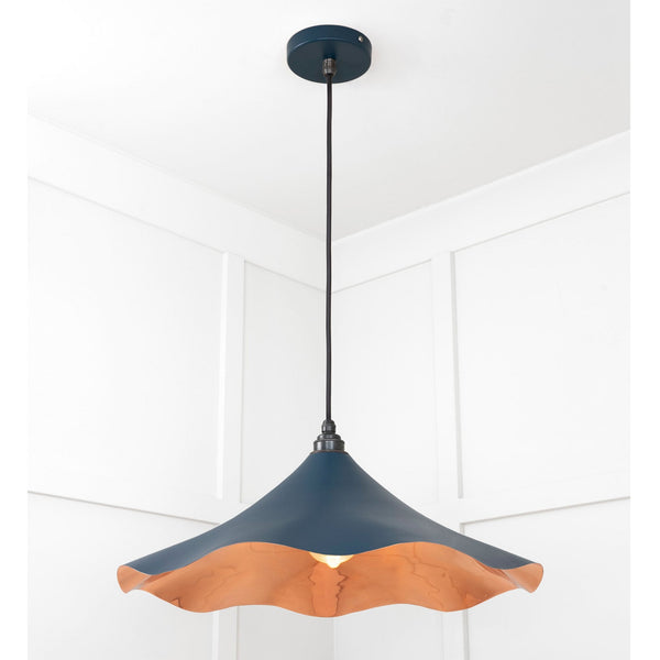 A dark blue and copper pendant light with a wavy rim hangs from a white ceiling.