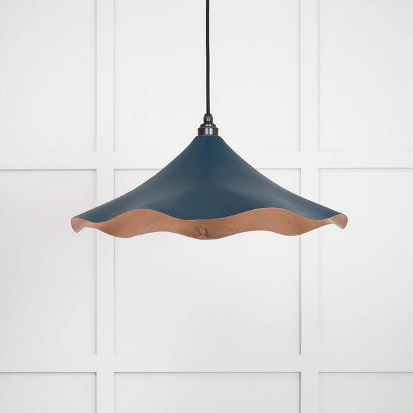 A dark blue and copper pendant light with a wavy rim against a white panelled wall.