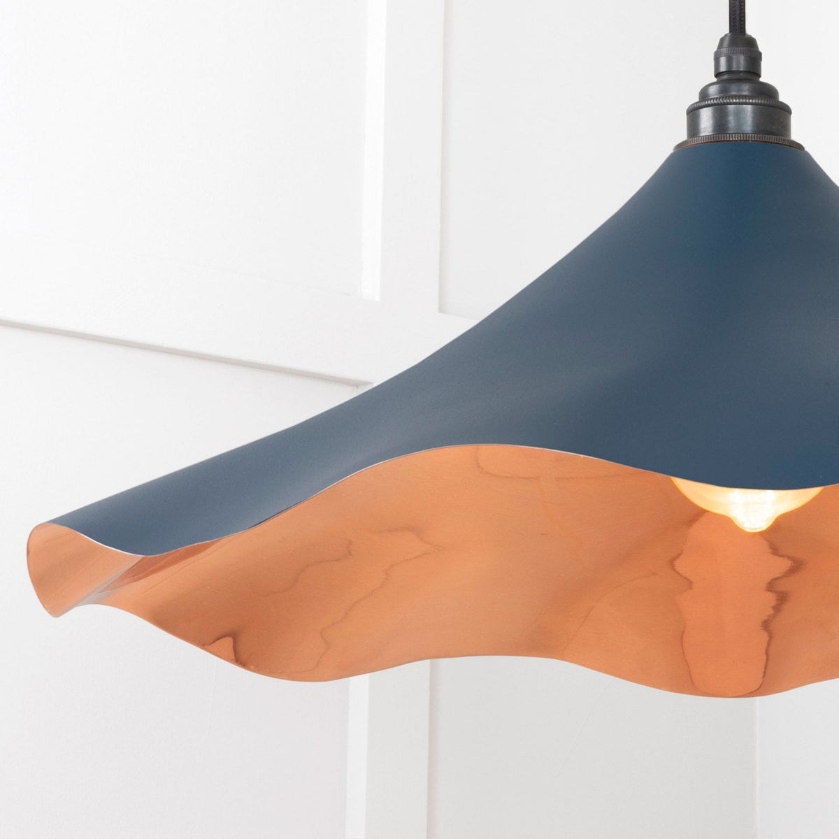 Close-up of the dark blue and copper pendant light's wavy rim, showing the inner glow.
