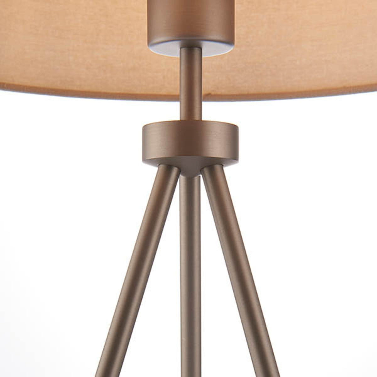 Close-up of the tripod base and stem of a table lamp with a beige shade.
